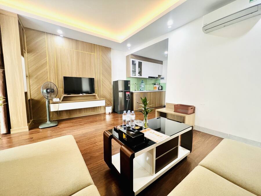 A modern living room with a flat-screen TV, a standing fan, and a coffee table with a magazine.