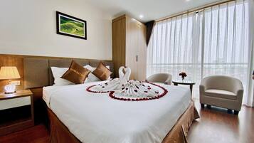 Habitación de hotel con una cama bien hecha, un cuadro enmarcado en la pared, una ventana con cortinas de gasa y una silla cerca de la ventana.
