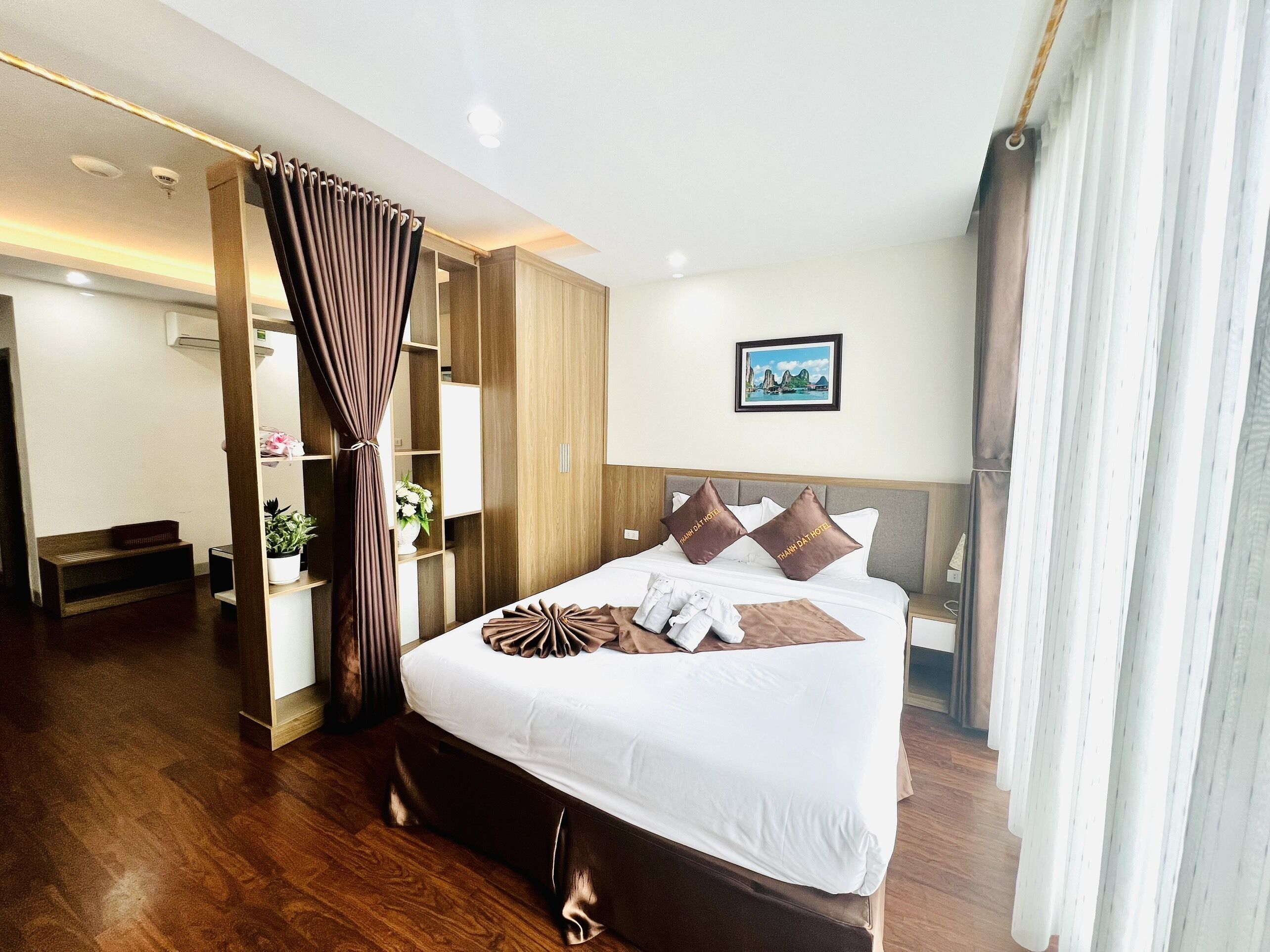 A hotel room with a large bed, wooden flooring, a wardrobe, a desk, and a bathroom.