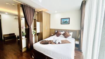 A hotel room with a large bed, wooden flooring, a wardrobe, a desk, and a bathroom.