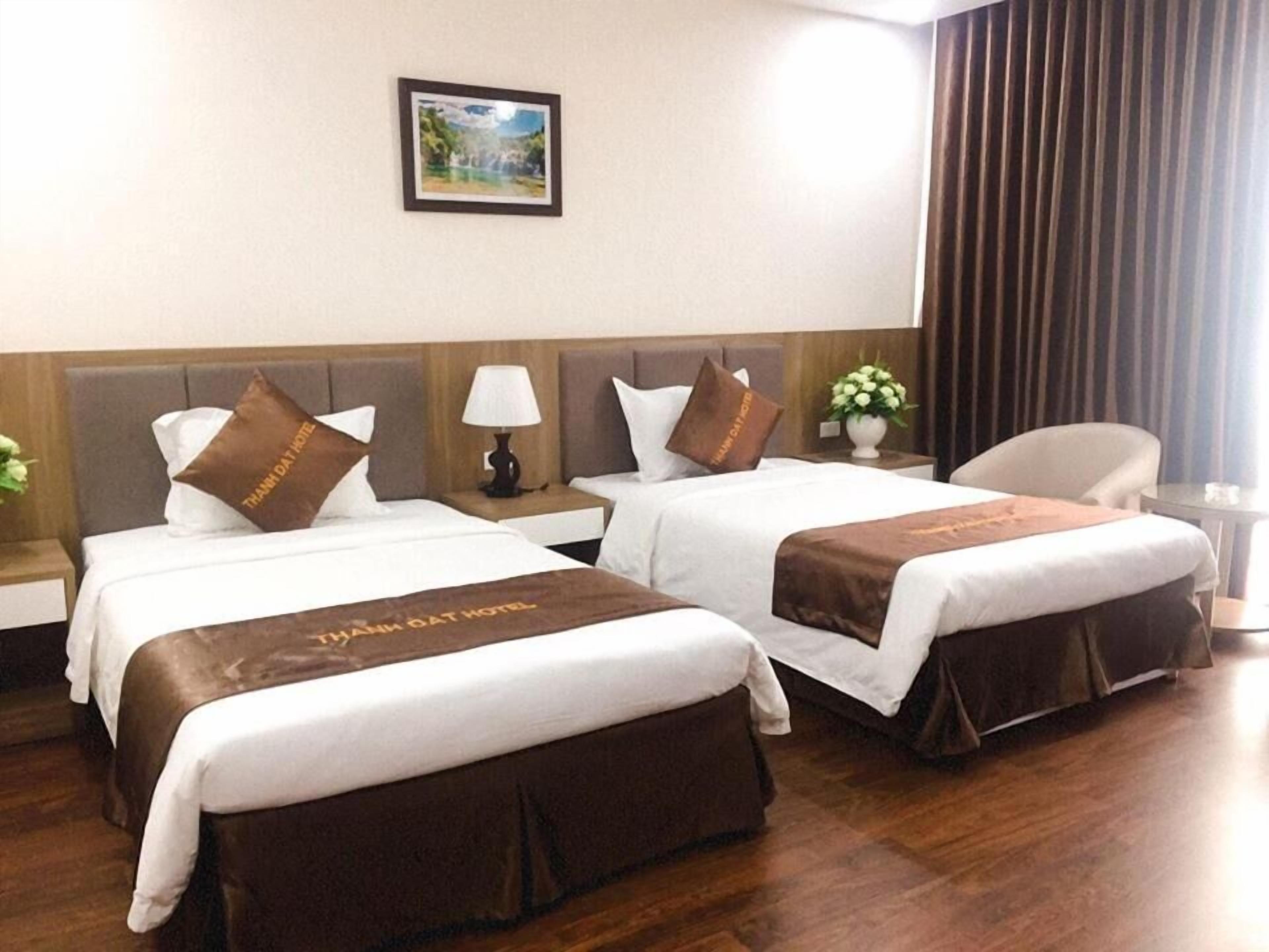 A hotel room with two beds, each with a brown bedspread and pillows, a nightstand with a lamp, and a framed picture on the wall.