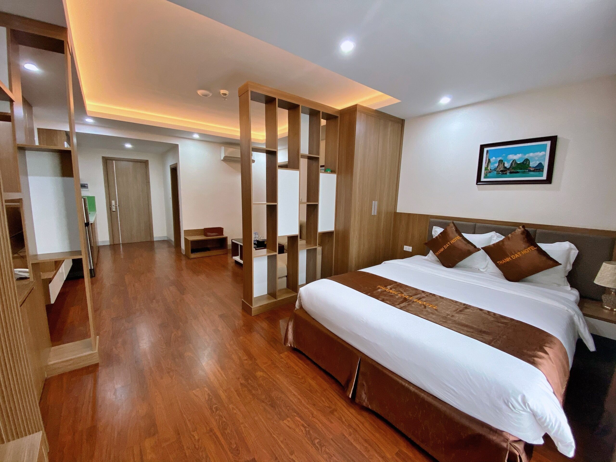 A hotel room with a large bed, wooden floor, and a view of the hallway.