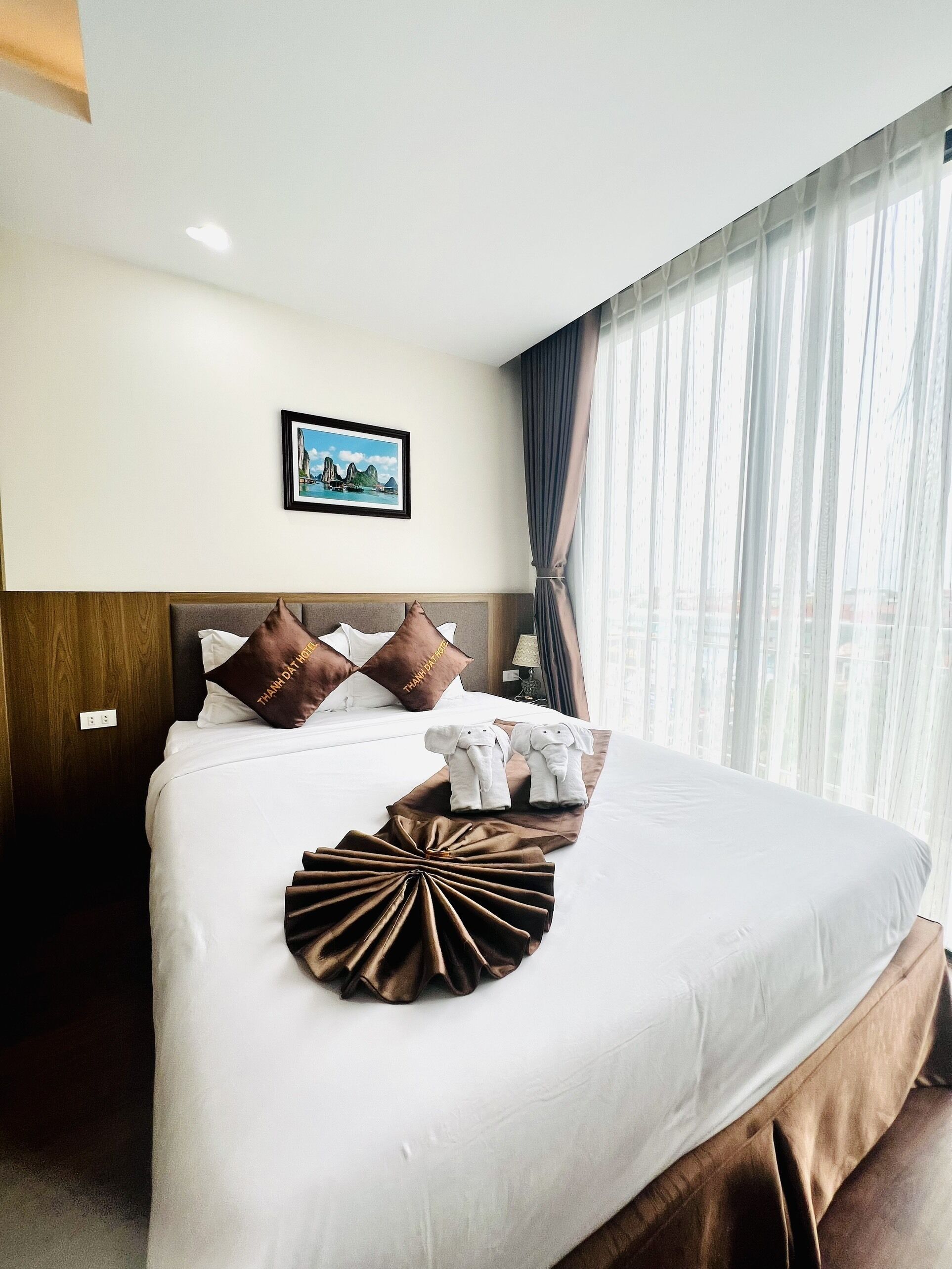 Ein Hotelzimmer mit einem ordentlich bezogenen Bett, einem gerahmten Bild an der Wand und einem Fenster mit Vorhängen.
