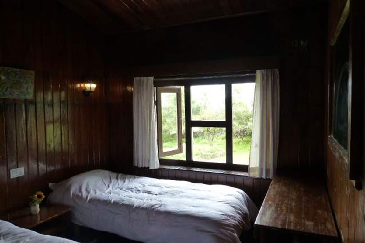 A room with wooden walls, a bed, a window with curtains, and a small table.