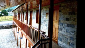 A covered outdoor area with a wooden railing, stone walls, and a view of a road and greenery. - Lukla Airport Resort, Lukla  (Lukla)