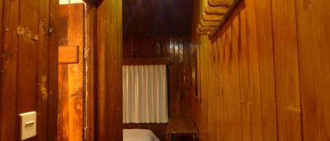 Un couloir étroit en bois, avec un lit au fond, une petite table et une poubelle verte.