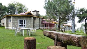 A stone house with a red roof, a dining area with chairs, and a large tree stump in the foreground. - Lukla Airport Resort, Lukla  (Lukla)