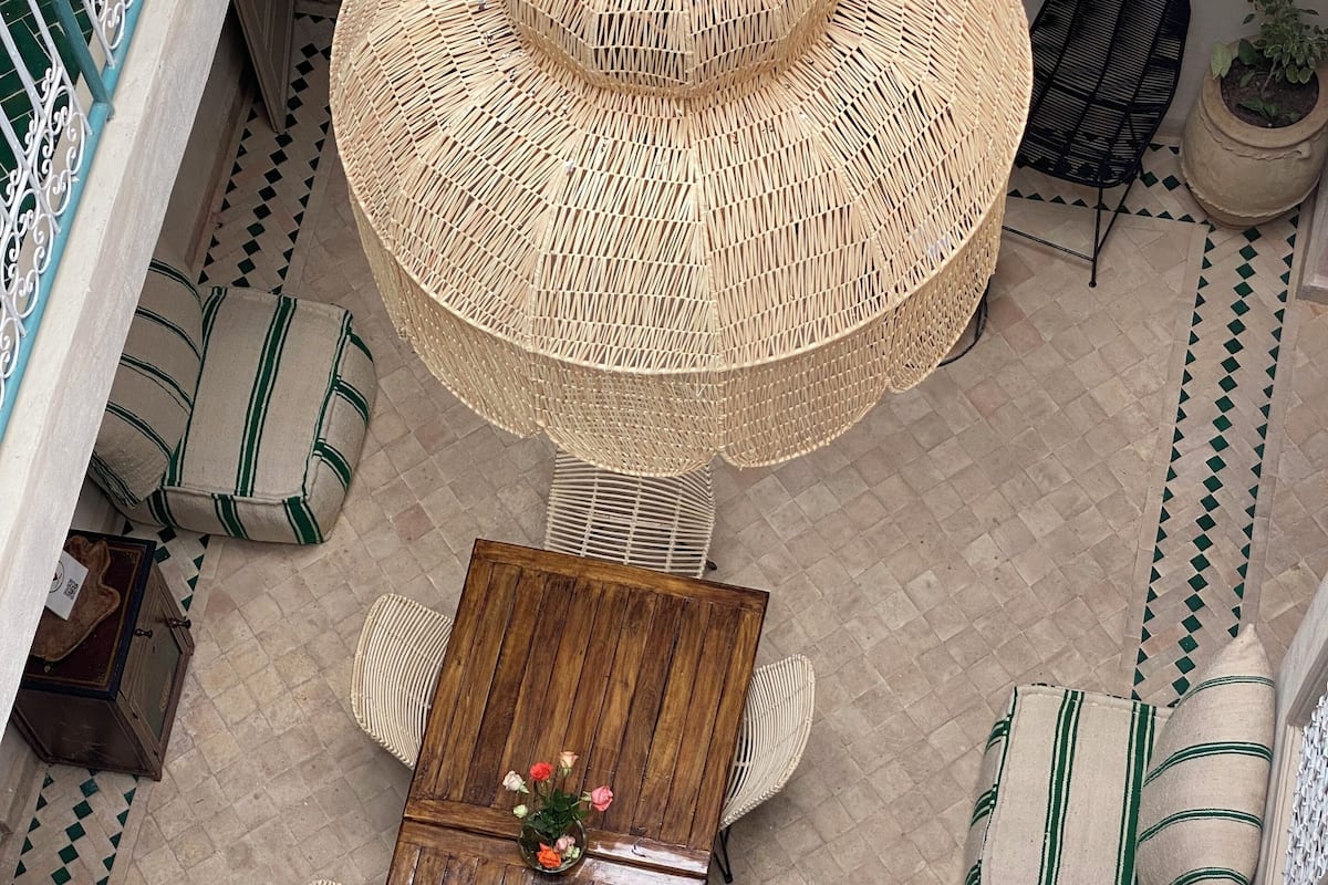A high ceiling with a large woven umbrella light fixture, a wooden table with chairs, and a patterned floor.