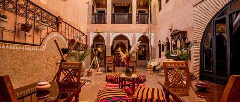 A traditional Moroccan interior with a courtyard, wooden furniture, and arches.