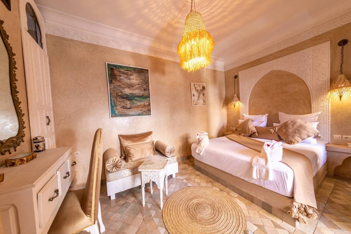 A spacious bedroom with a large bed, a sitting area with a chair and table, and a decorative mirror.
