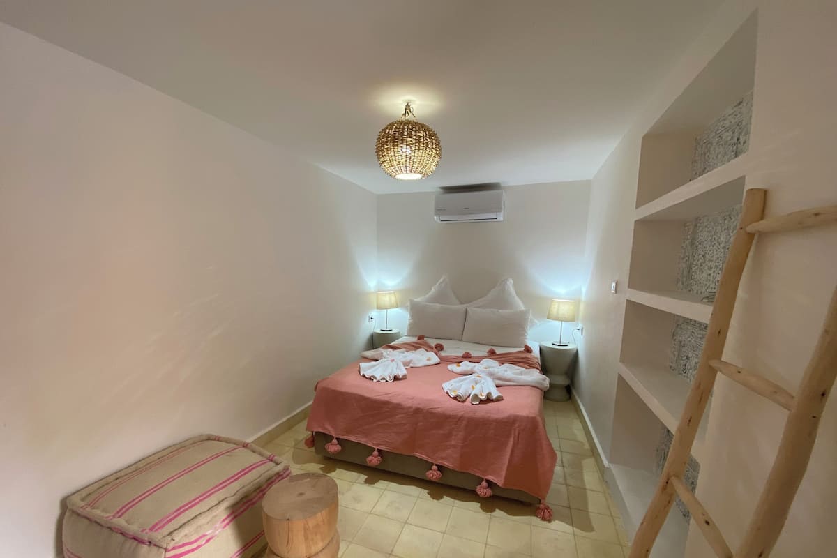 A bedroom with a bed, bedside lamps, a wooden stool, a ladder, and a decorative ceiling light.