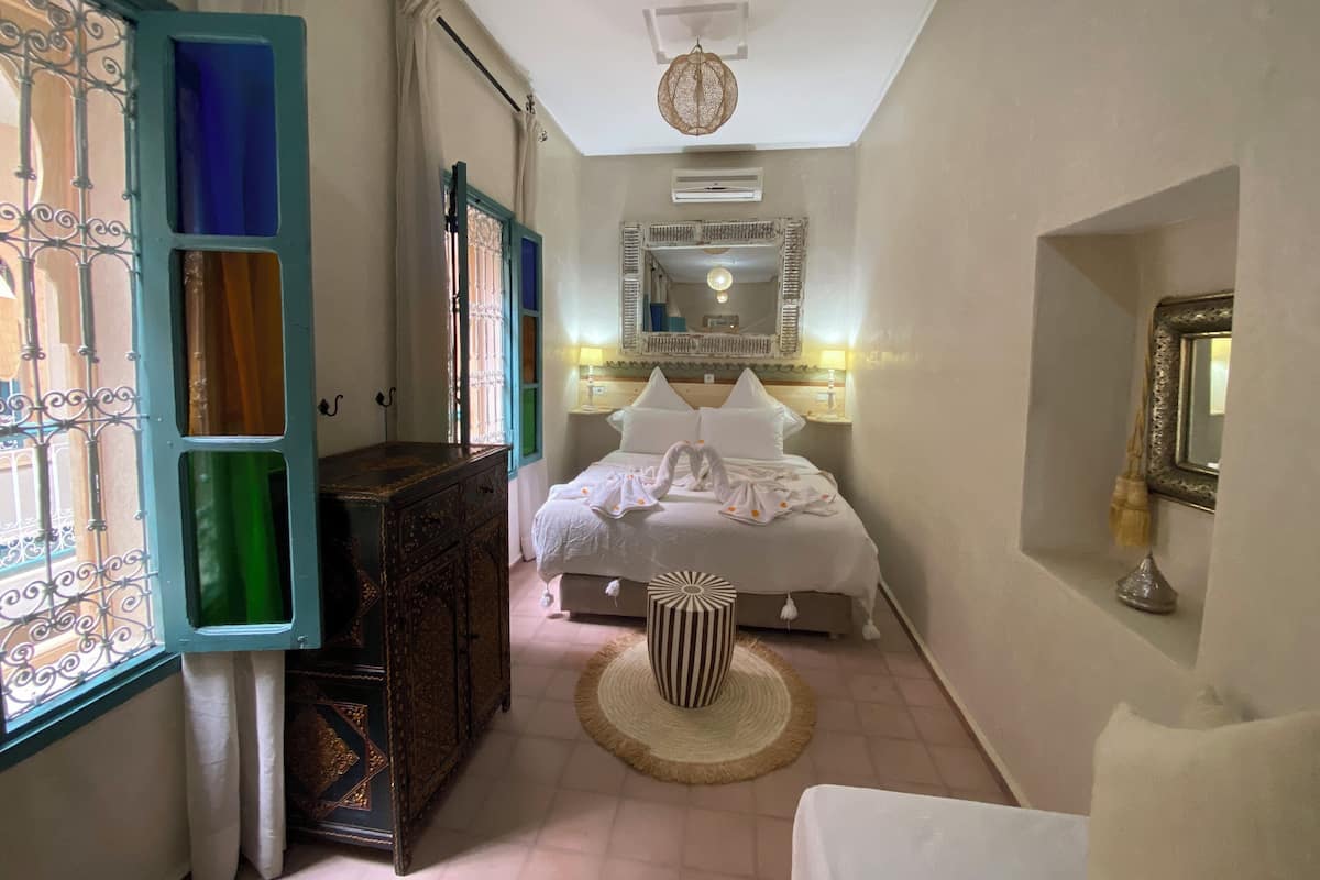 A bedroom with a bed, a dresser, a round ottoman, and a mirror on the wall.
