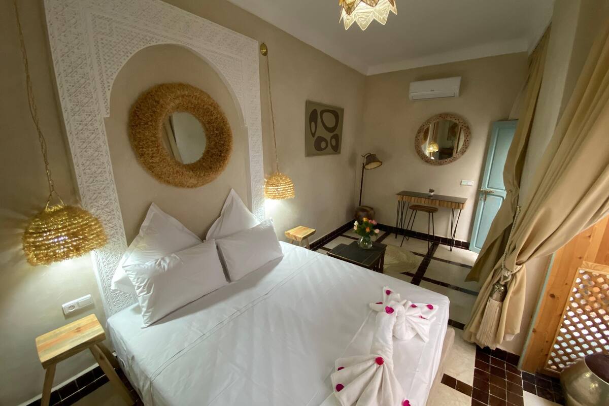 A hotel room with a large bed, a small table, a mirror, and a desk.