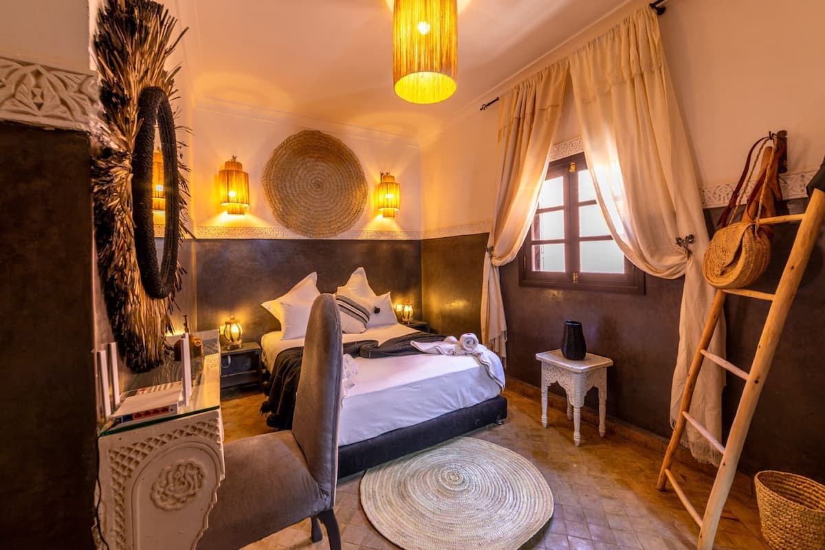 A cozy bedroom with a bed, bedside lamps, a woven wall hanging, a wooden ladder, and a woven rug.