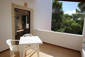 A balcony with a white table and chairs, a door leading to an interior room, and a view of trees.