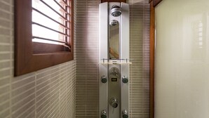 Ein Badezimmer mit einer Duschkabine, einem Fenster mit Jalousien und gefliesten Wänden.
