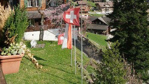 A wooden house with a Swiss flag, a mountain backdrop, and a small garden. - Hotel Sonnenberg (Grindelwald)