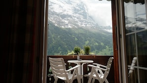 A balcony with a table and chairs, overlooking a mountainous landscape with snow-capped peaks and lush greenery. - Hotel Sonnenberg (Grindelwald)