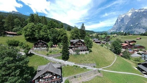A mountain village with traditional wooden houses, a central building with a sign that reads "Hotel Sonvensberg," and a railway track running through the village. - Hotel Sonnenberg (Grindelwald)