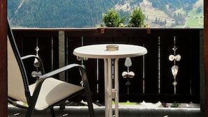 A balcony with a wooden floor, a round table, and two chairs. It overlooks a mountainous landscape with snow-capped peaks and dense forests. - Hotel Sonnenberg (Grindelwald)