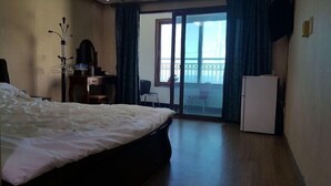 Ein Hotelzimmer mit Bett, Schreibtisch, Stuhl, Kühlschrank und einem Balkon mit Blick.