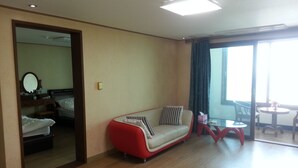 Ein Hotelzimmer mit einem Bett, einem rot-weißen Sofa, einem kleinen Tisch und einem großen Fenster mit Vorhängen.