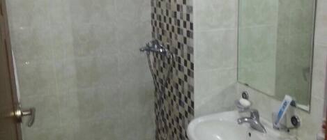 A bathroom with a shower, toilet, sink, and a tiled wall with a checkered pattern.