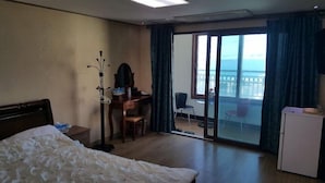 A hotel room with a bed, a desk, a chair, and a view of the sea through a sliding door. - Eden Hostel (Jeju City)