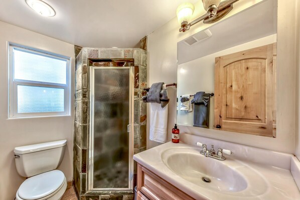 A bathroom with a glass shower enclosure, a white toilet, a sink with a mirror, and a wooden cabinet.