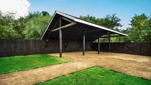 Un espacio al aire libre techado con un sendero de tierra y césped verde, rodeado por una valla de madera.