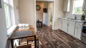 Una cocina con suelo de madera, armarios blancos, una mesa de comedor con un florero y un reloj en la pared.