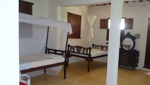 A room with two wooden beds, a white canopy bed, a wooden chair, a small table, and a mirror on a dresser. - Dudu Villas n Cottages (Lamu)