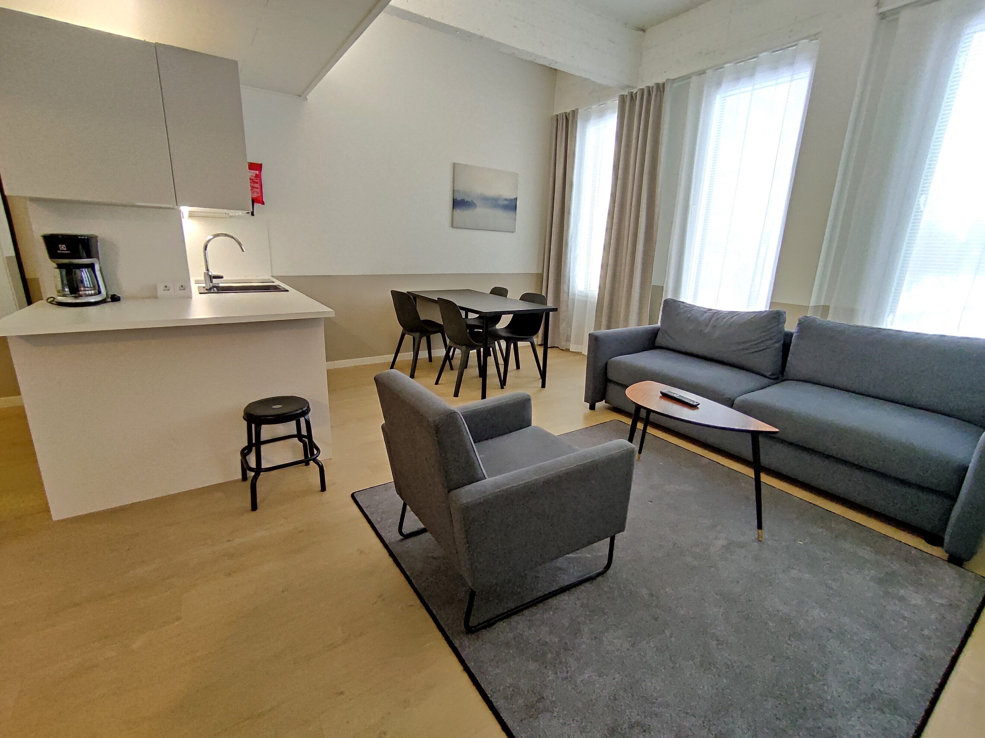 A modern living room with a grey sofa, a small coffee table, and a dining area with a table and chairs.