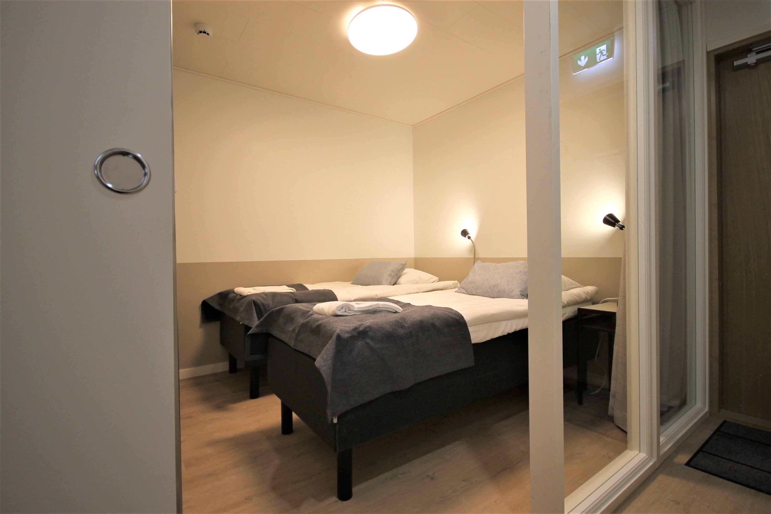 Ein Hotelzimmer mit zwei Betten, einem Nachttisch, einer Lampe und einer Tür mit Glasfenster.