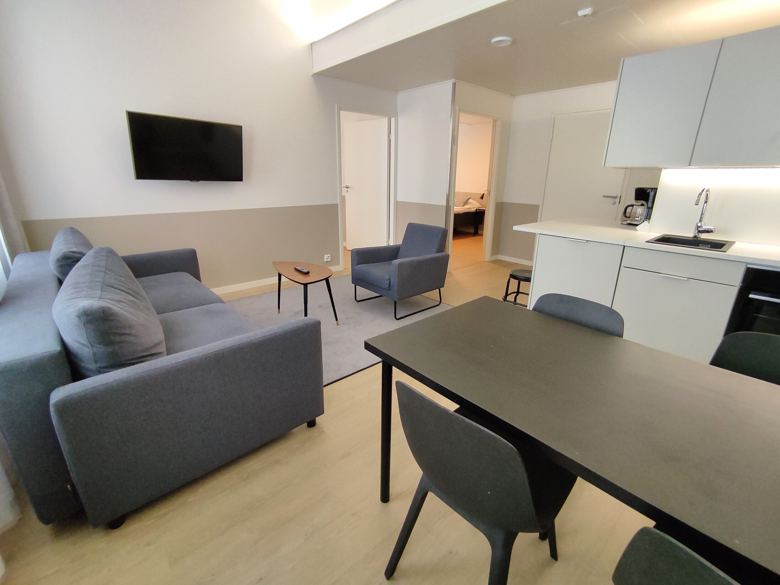 A modern living space with a grey sofa, a small table, and a dining area with chairs.