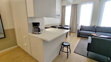 A modern kitchen with a coffee maker, a dining area with a sofa and a small table, and a large window with curtains.