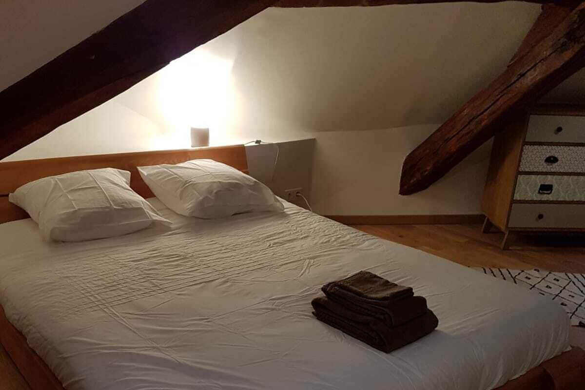 Une chambre à coucher avec un cadre de lit en bois, du linge de lit blanc et une petite table de chevet avec une lampe.