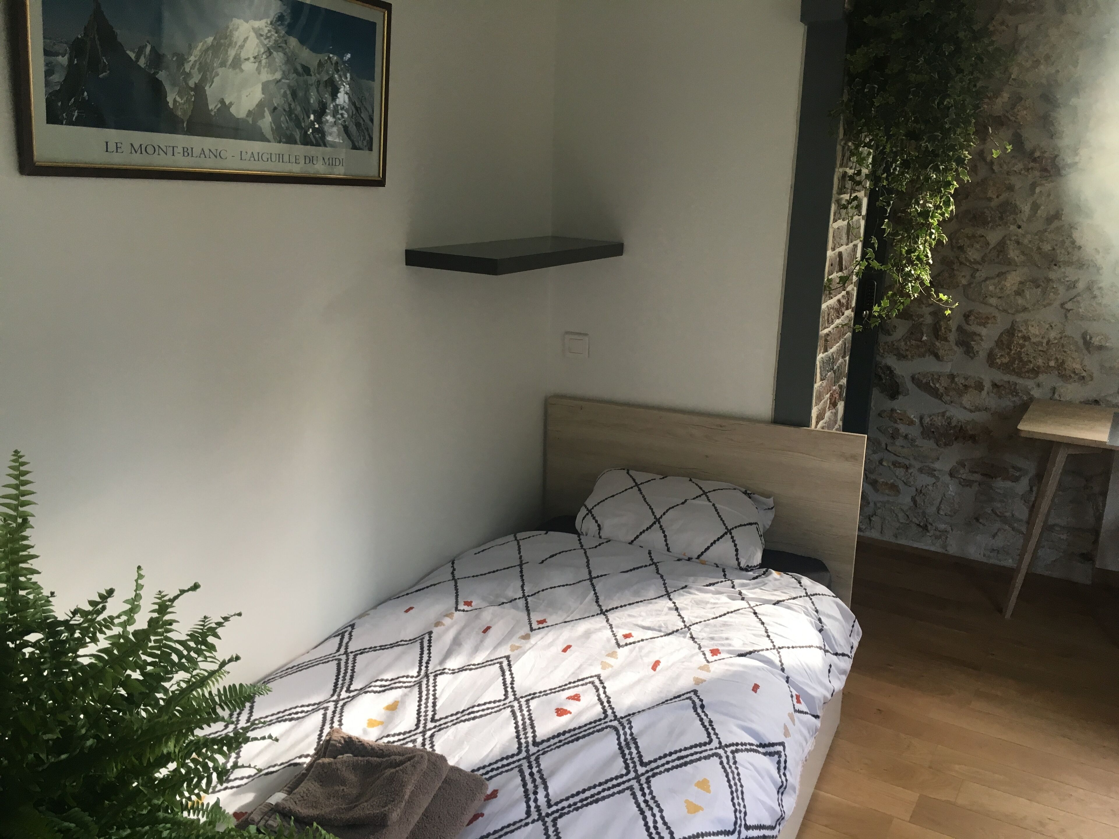 Un dormitorio con cama, un cuadro enmarco de Mont Blanc, pared de piedra y una pequeña estantería.