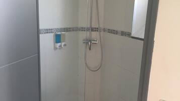 Un petit espace douche fermé, comprenant des toilettes, un sol carrelé et un distributeur de savon fixé au mur.