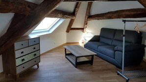 A loft-style room with exposed wooden beams, a sofa, a small table, and a dresser. - Les chambres d'Orsay (Orsay)
