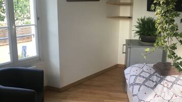 Une pièce comprenant un lit, une chaise, une plante en pot et un tableau accroché au mur.