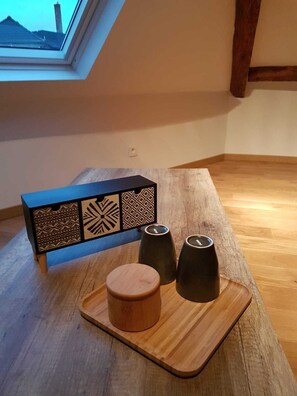 Uma mesa de madeira com uma bandeja, uma caixa decorativa e dois objetos pretos sobre um chão de madeira com uma claraboia.