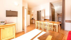 Un espace de vie compact comprenant un coin cuisine, un coin repas avec des meubles en bois et un téléviseur fixé au mur.