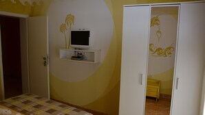 Um quarto com uma cama, um guarda-roupa, uma televisão em uma estante e um detalhe decorativo na parede.