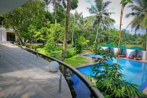 A swimming pool surrounded by lush greenery and palm trees, with a covered seating area and a pathway leading to a building. - Green Residences Galle (Bope-Poddala)