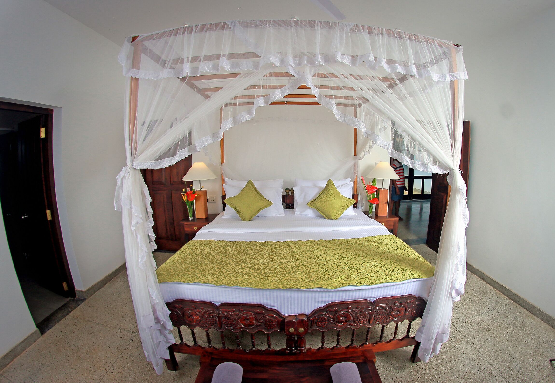 A four-poster canopy bed with a green bedspread, two pillows, and a nightstand with a lamp.