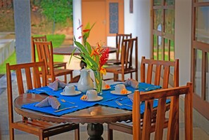 A dining table set with blue placemats, white cups, and a vase with flowers.