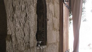 Un mur de pierre avec une petite fenêtre en arc de cercle et une porte en bois surmontée d’un rideau.