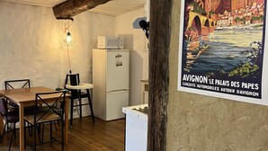 Une cuisine chaleureuse avec des poutres en bois, un coin repas avec une table et des chaises en bois, un réfrigérateur blanc et un luminaire fixé au mur.