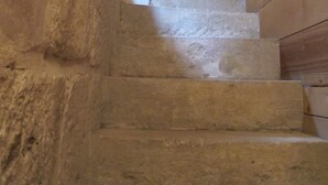 Un escalier en bois, avec un mur en pierre d’un côté et un lambris en bois de l’autre.